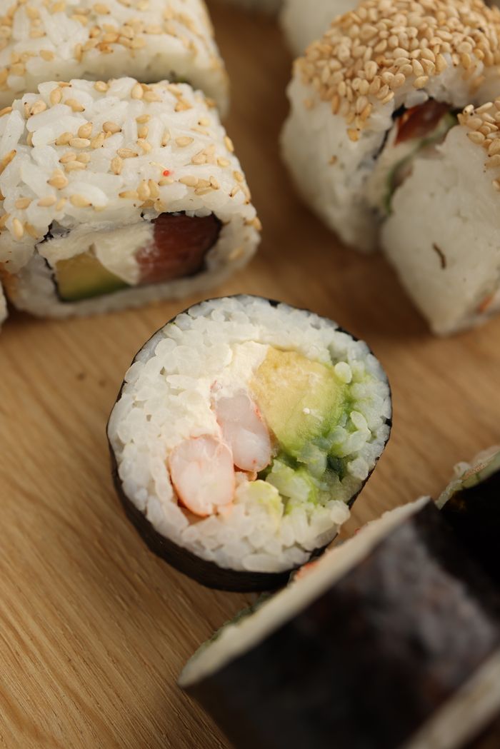 Close-up of sushi rolls featuring fresh avocado and seafood on a wooden board.